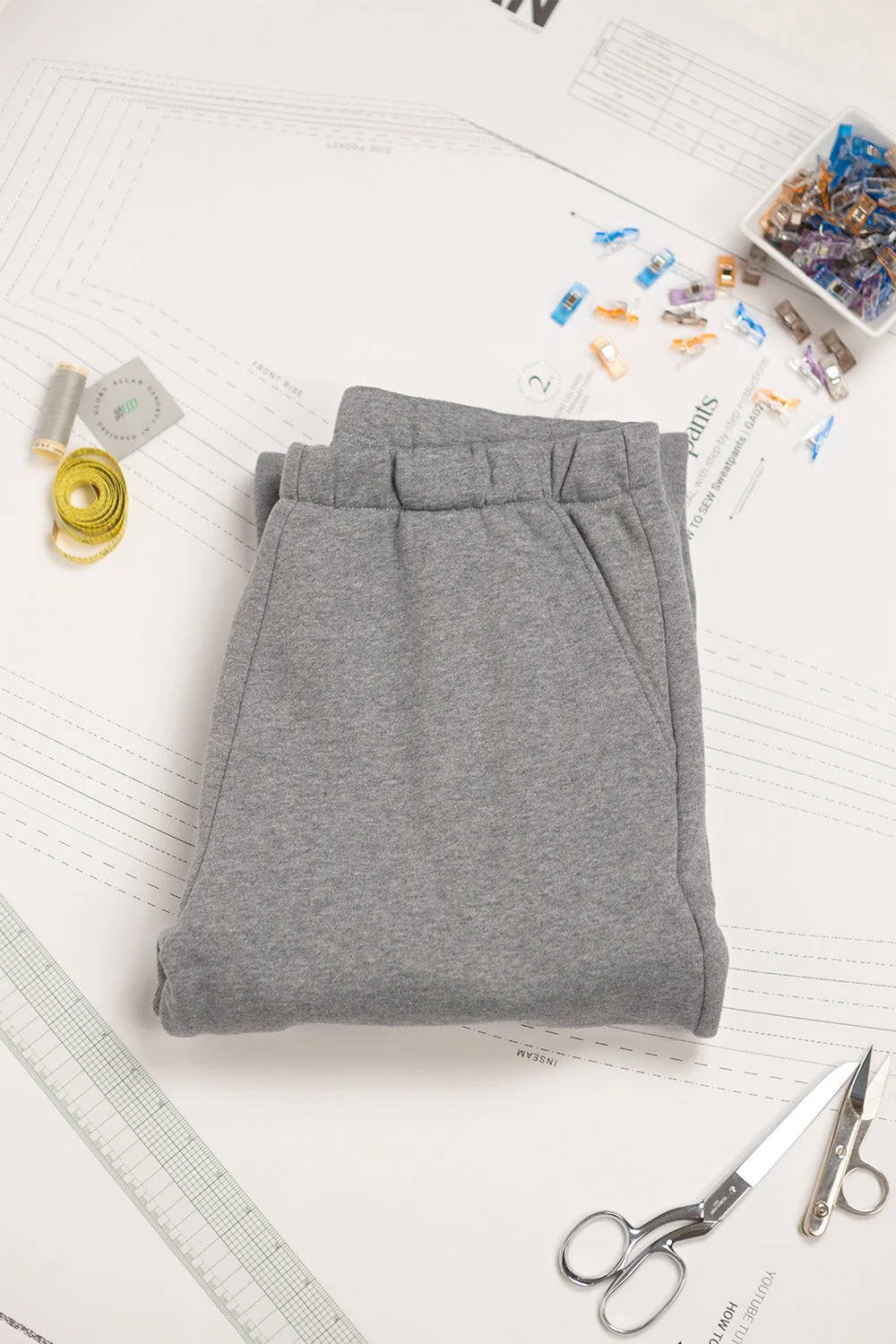 Folded gray pants on a white surface with sewing tools and materials.