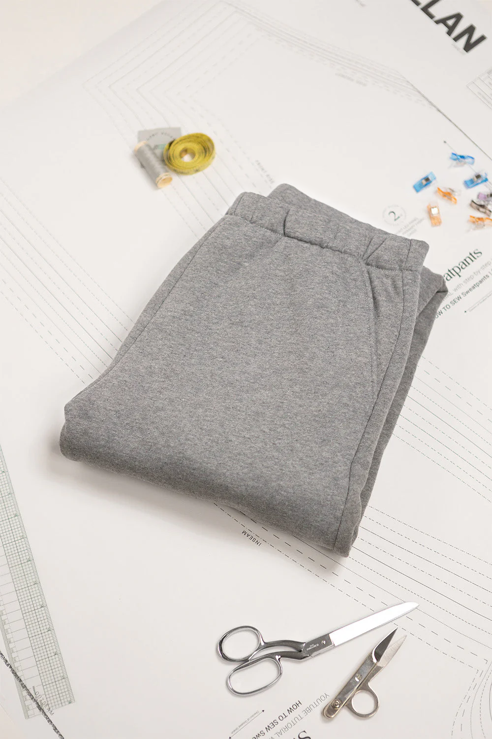Folded gray pants on a newspaper with scissors and measuring tape.
