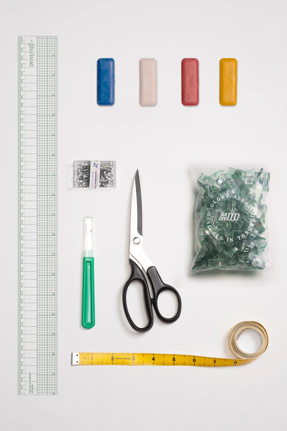 Crafting tools including scissors, ruler, tape measure, and small containers on a white background