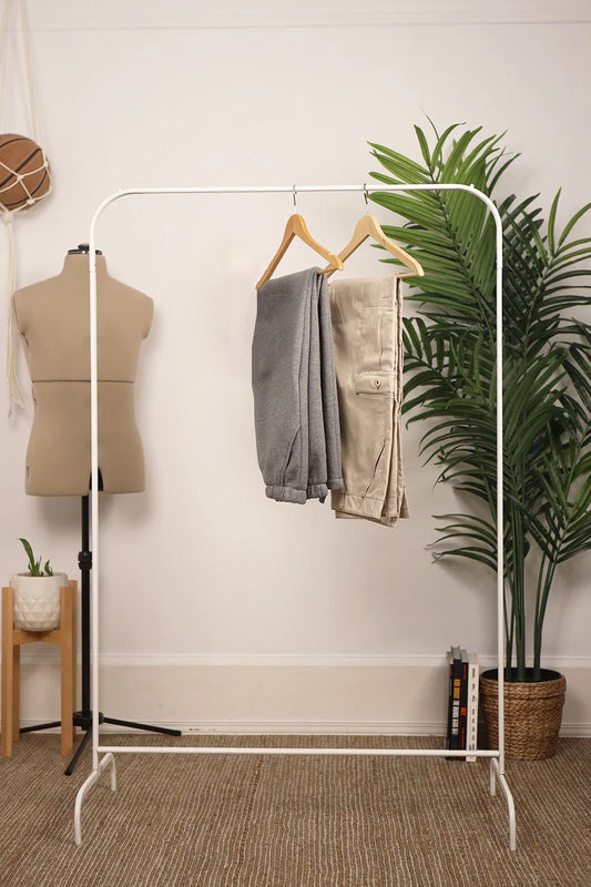 White clothing rack with pants, mannequin, and plants in a room setting. Sweatpants and cargo pants hanging.