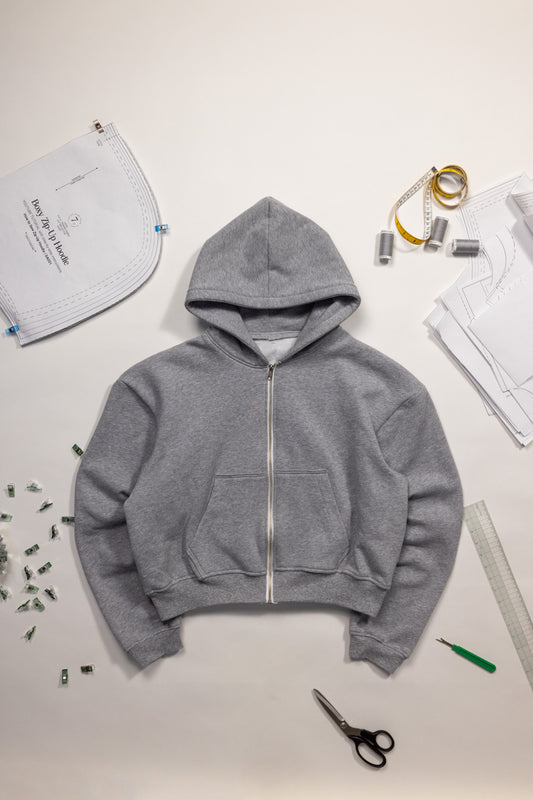 Gray boxy zip-up hoodie on a white surface with sewing tools and materials