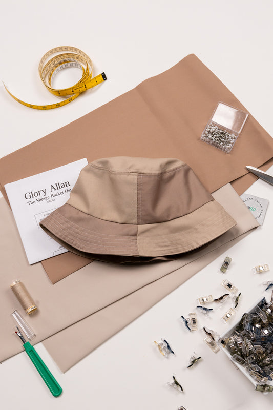 Brown bucket hat on a white surface with sewing materials and tools.