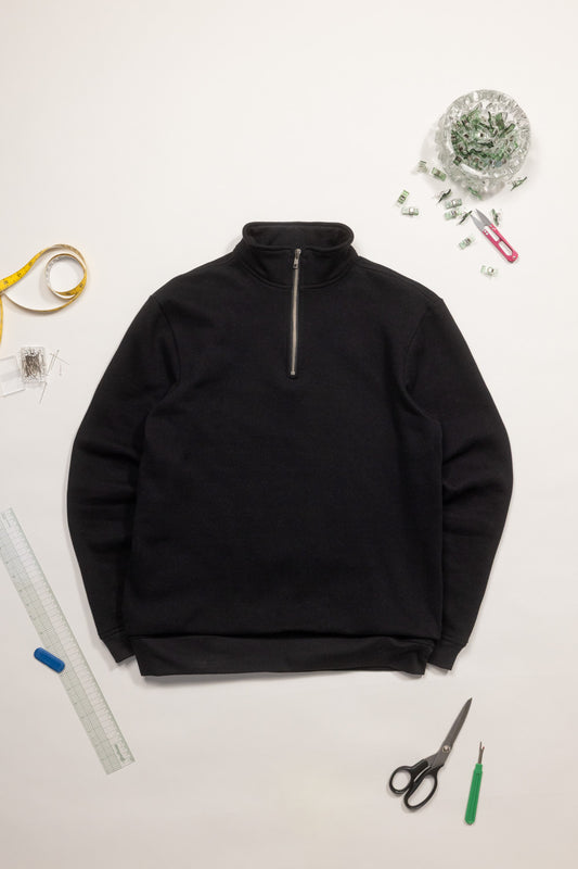 Black half-zip sweatshirt on a white surface with sewing tools.