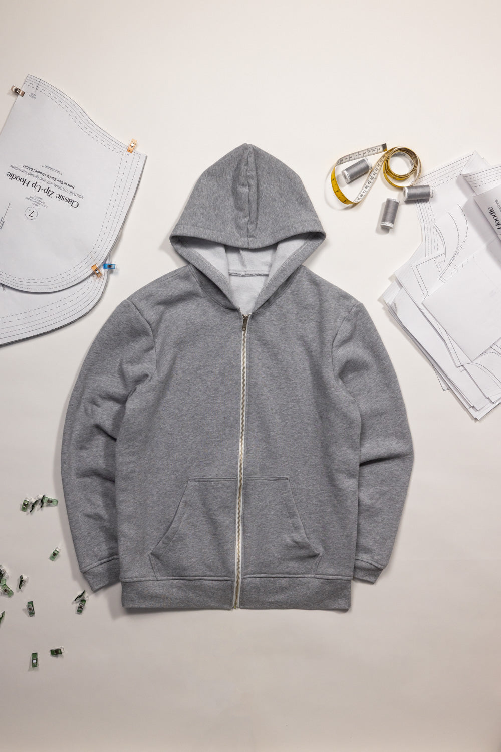 Gray hoodie on a light beige surface with various sewing items around