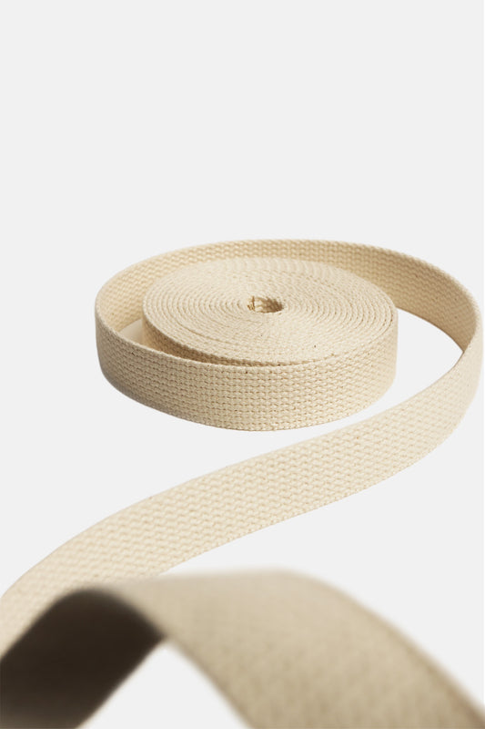 A roll of 1.5", natural-beige 100% cotton webbing, rolled up on a white background.