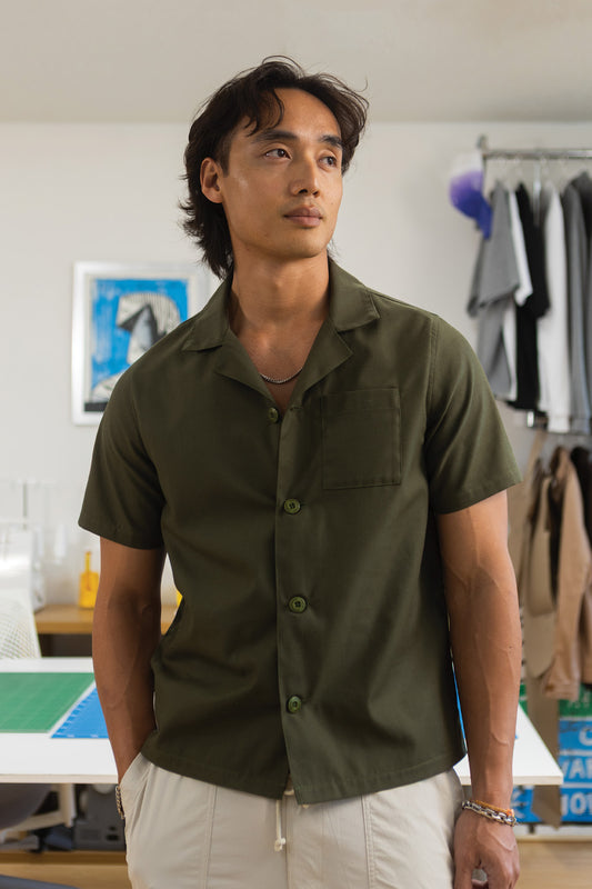 Man wearing a green shirt standing in a room with clothes in the background