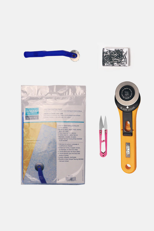 Collection of sewing tools including a rotary cutter, scissors, and a package on a white background